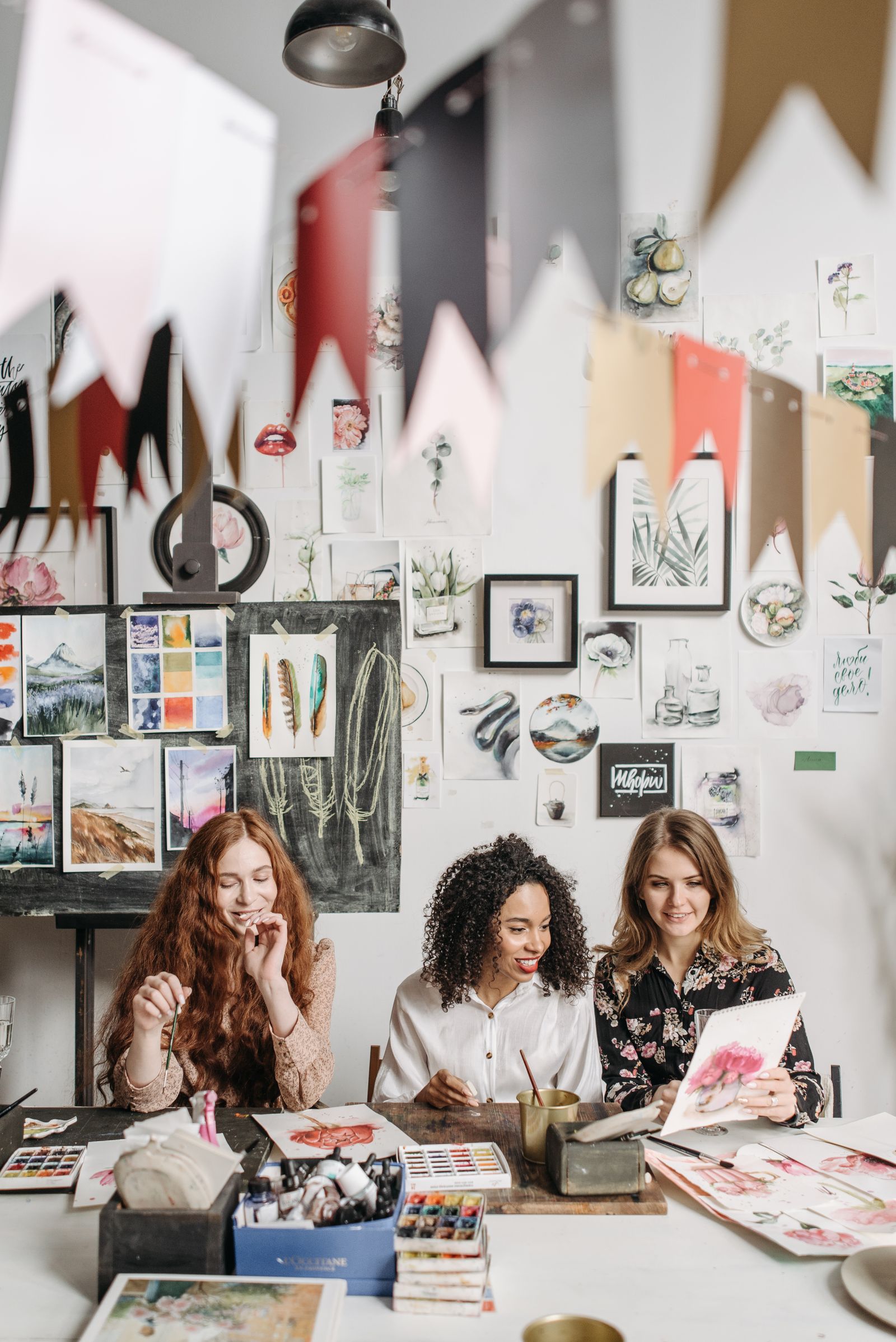 Stock photo of three women sharing a painting at a table with brushes and watercolors.
